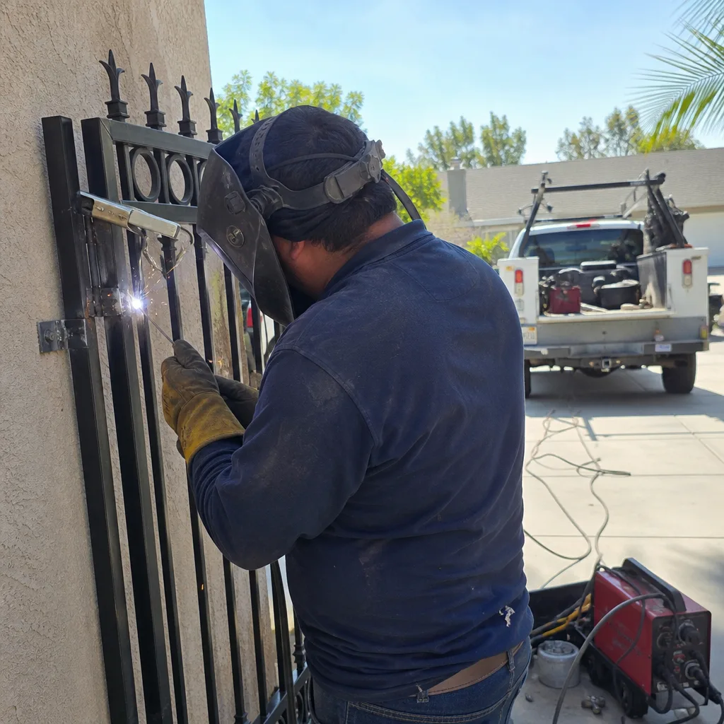 Professional welder performing metal gate repair with safety equipment